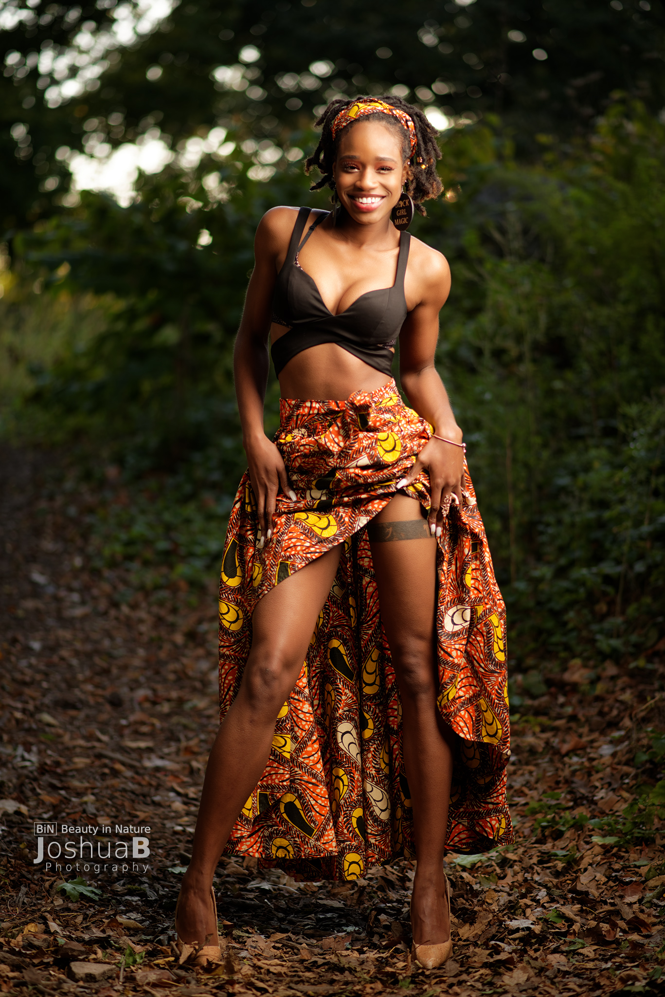 Beautiful black woman with dreadlocks lifting African print skirt to reveal leg tattoo