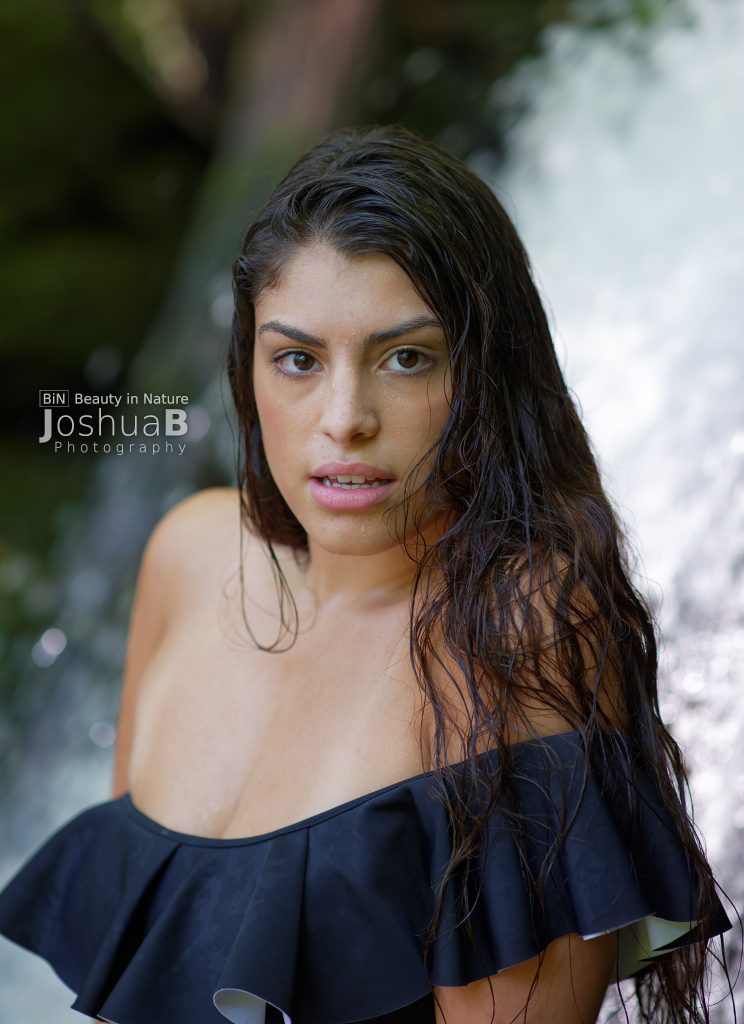 Beautiful young woman posing in front of waterfall dark blue bikini
