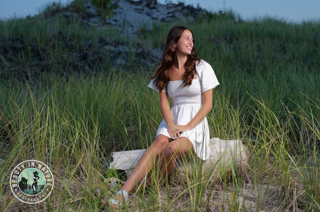 Hanna in short white dress sitting on log in sand dunes at Hampton Beach