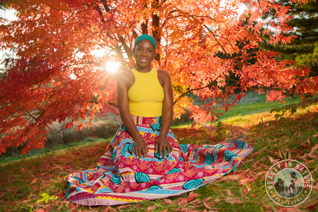 Kneeling beautiful young Haitian woman in African skirt and yellow tank top tree sunset fall foliage