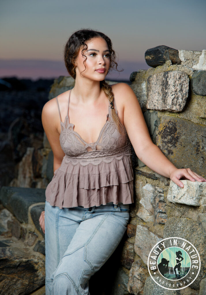 Beautiful high school senior girl wearing halter top and jeans posing against a wall near ocean
